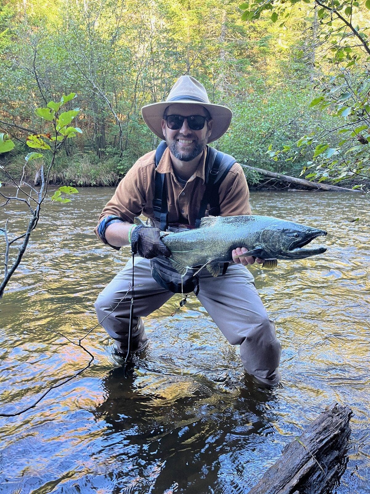 An angler in a brimmed hat standing in the river holding a Chinook salmon
