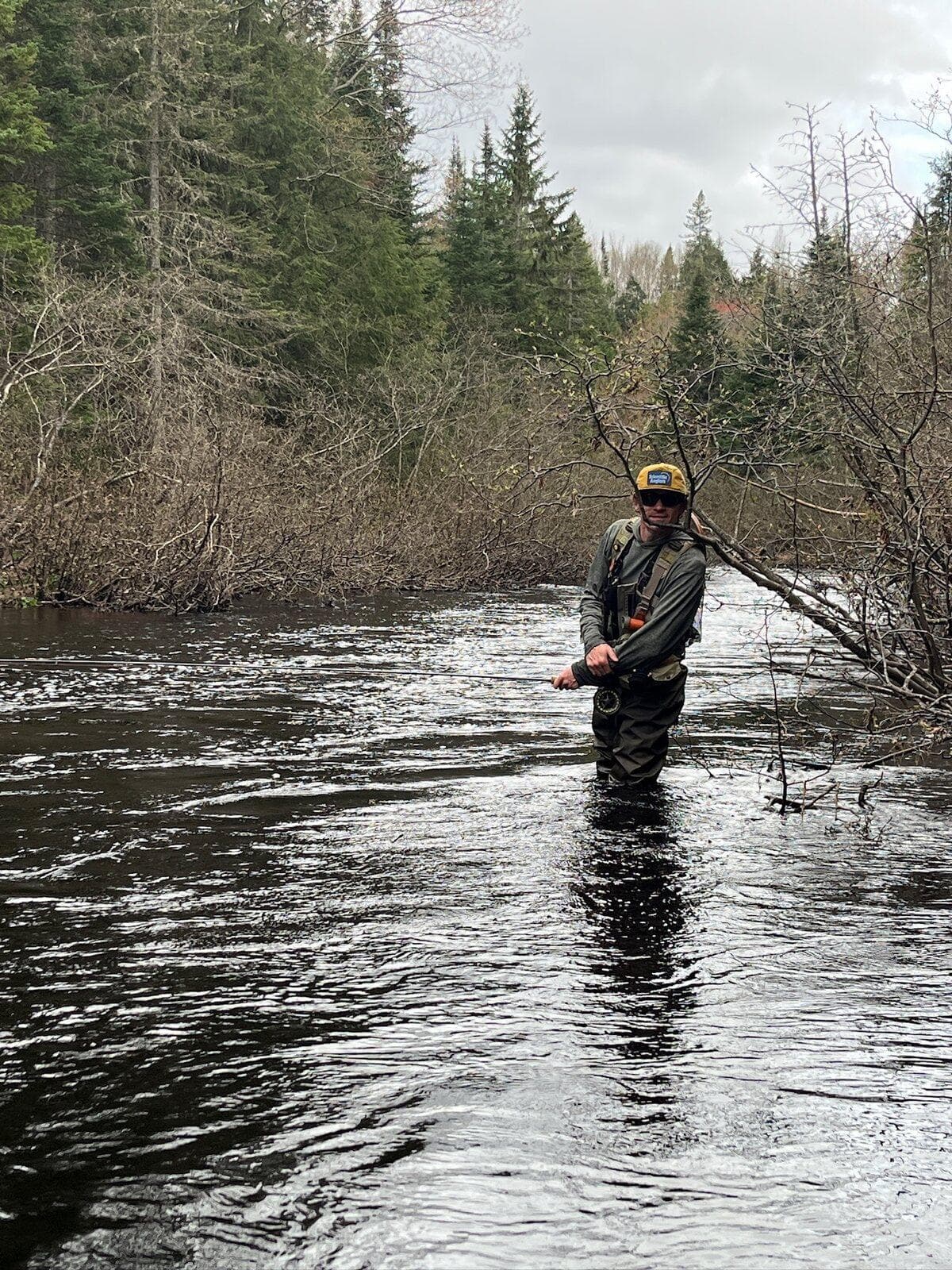 A distant angler wading a wide river bend with a low spring sky